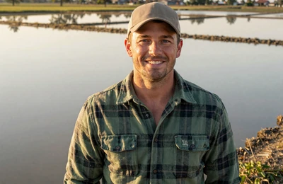 Travis, 38, Arkansas rice farmer from Stuttgart smiling in a golden-hour rice field on Yougotmatched