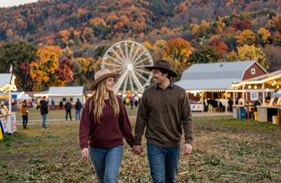 Couple walking through an Appalachian county fair at twilight with string lights and livestock barns