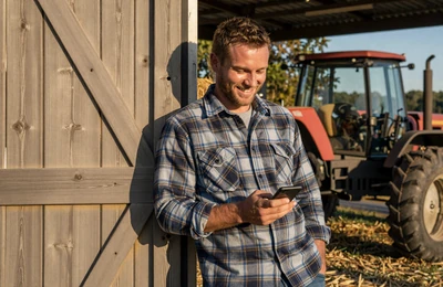 Farmer smiling at his phone while leaning against a barn door in warm afternoon light on a Southern farm