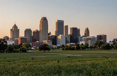 Kansas City Missouri skyline at dusk with surrounding green farmland and rolling hills in the distance