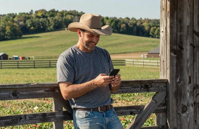 Farmer smiling at his phone leaning against a barn door on a Missouri farm in warm afternoon light