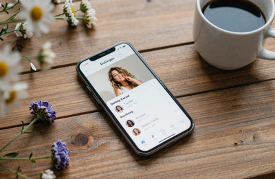 Smartphone showing farmer dating profile on rustic farmhouse table with coffee and wildflowers