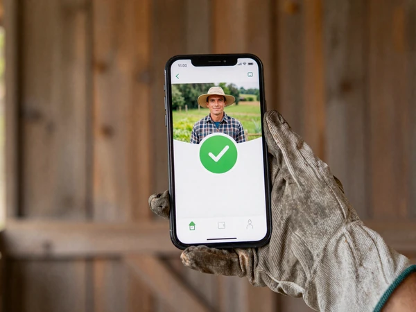 Farmer holding smartphone showing verified profile badge on Yougotmatched dating platform
